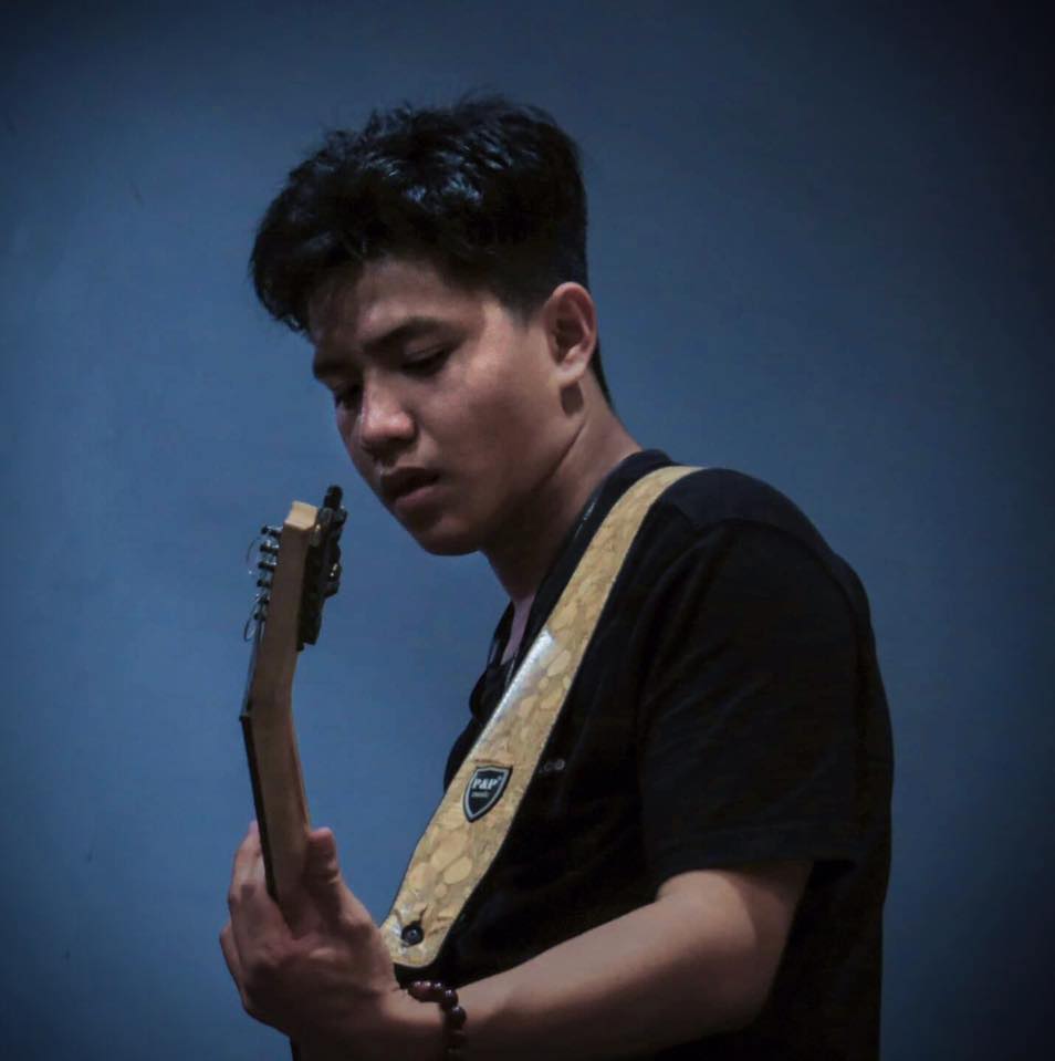 A portrait in low blue light: a musician looking down at a guitar mid-phrase.